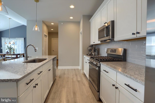 kitchen with light wood-type flooring, decorative backsplash, stainless steel appliances, white cabinetry, and a sink