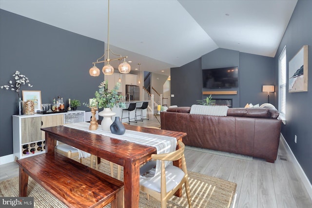 dining room with stairway, baseboards, light wood-style flooring, and vaulted ceiling