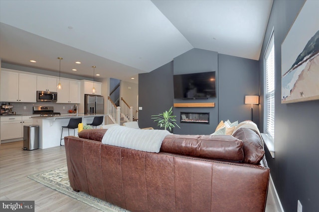 living room with stairway, light wood-style flooring, recessed lighting, vaulted ceiling, and a glass covered fireplace