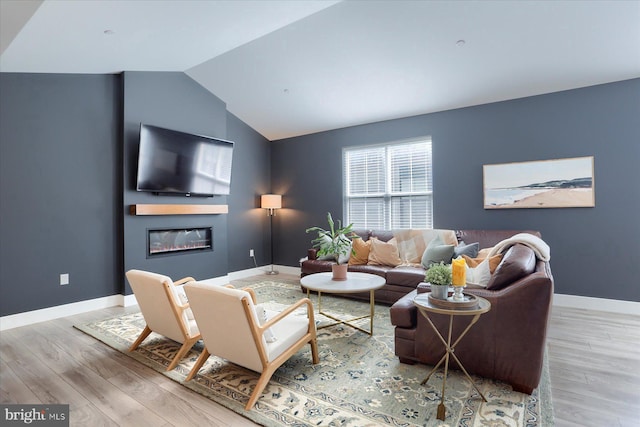 living area with a glass covered fireplace, lofted ceiling, wood finished floors, and baseboards