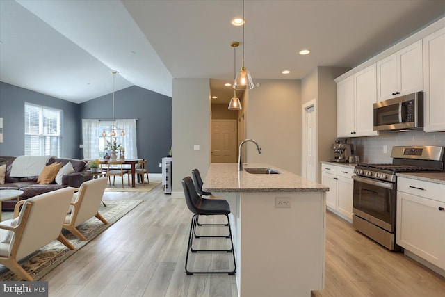 kitchen featuring light wood-style flooring, a sink, open floor plan, appliances with stainless steel finishes, and tasteful backsplash