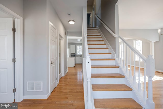 stairway with visible vents, wood finished floors, arched walkways, decorative columns, and baseboards