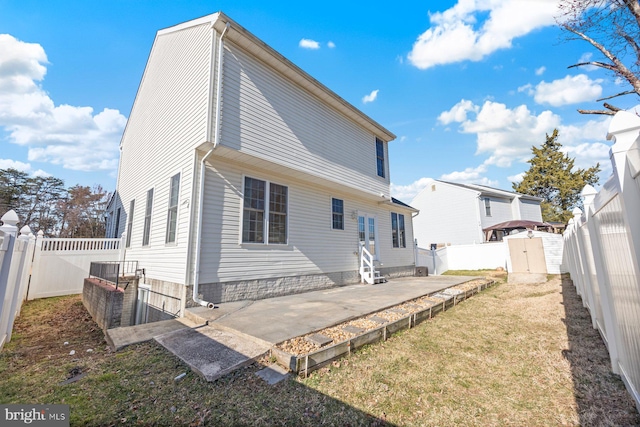 back of house featuring entry steps, a lawn, an outdoor structure, a fenced backyard, and a patio area