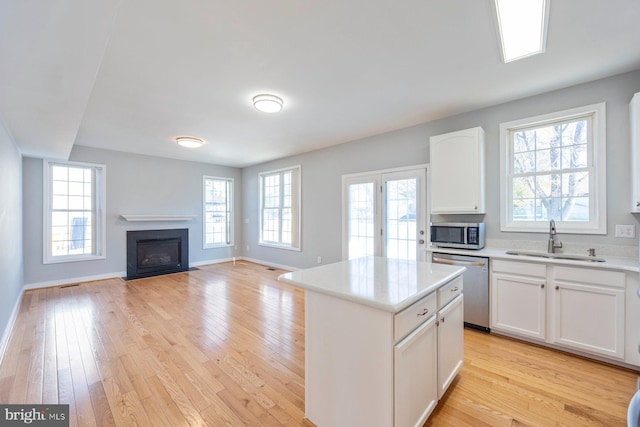 kitchen with light wood finished floors, a fireplace with flush hearth, stainless steel appliances, and a sink