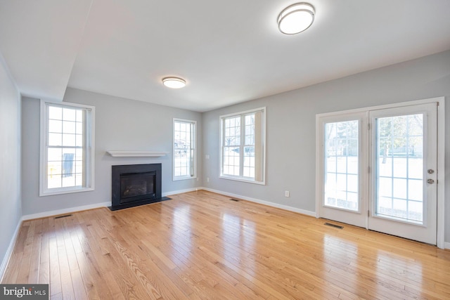 unfurnished living room with visible vents, baseboards, light wood-type flooring, and a fireplace with flush hearth