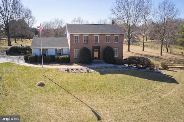 colonial home featuring brick siding, a chimney, a front yard, and fence