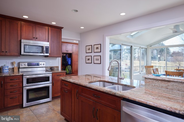 kitchen with a sink, a ceiling fan, light stone countertops, and stainless steel appliances