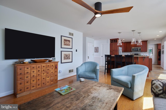 living area with light wood-type flooring, a ceiling fan, visible vents, and baseboards