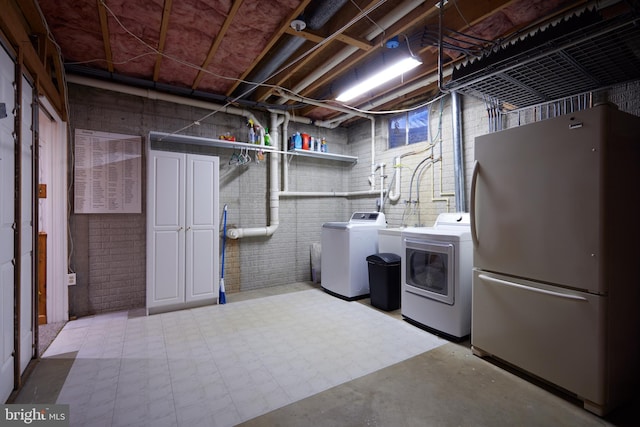 unfinished below grade area featuring washer and clothes dryer, brick wall, and freestanding refrigerator