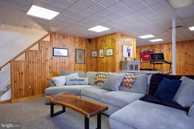 carpeted living room with baseboards, wood walls, and stairs