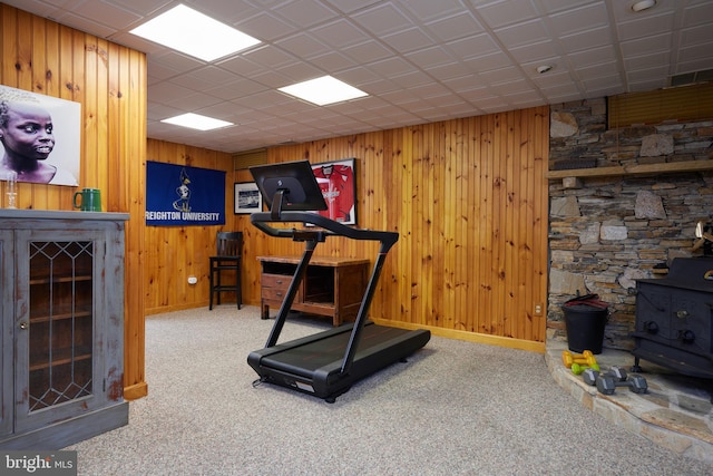 exercise area with a wood stove, carpet flooring, baseboards, and wood walls