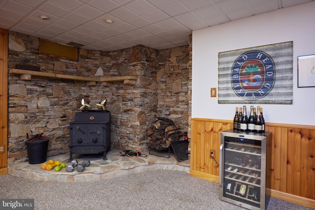 carpeted living area with wine cooler, wooden walls, wainscoting, and a wood stove