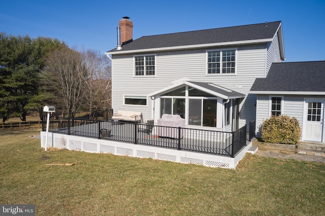 rear view of property featuring a deck, a sunroom, a yard, a shingled roof, and a chimney