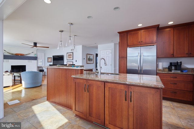 kitchen featuring light stone countertops, a center island with sink, a sink, stainless steel refrigerator, and open floor plan