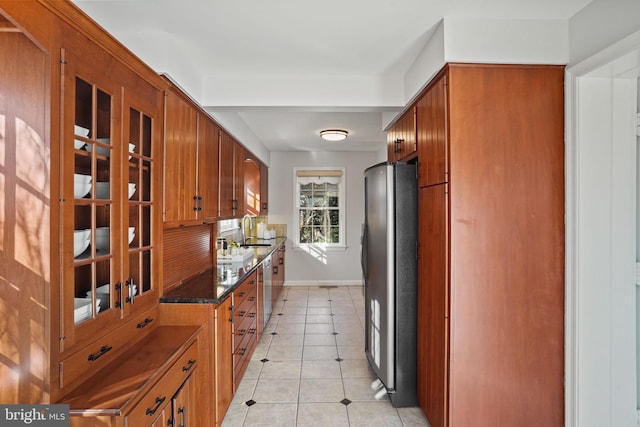 kitchen featuring light tile patterned floors, glass insert cabinets, brown cabinetry, and freestanding refrigerator