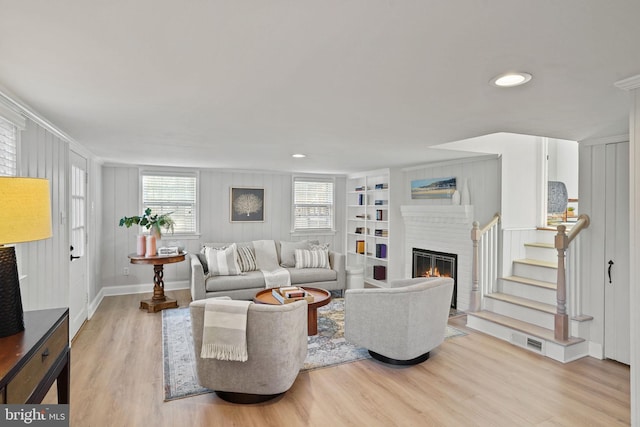 living area featuring visible vents, built in shelves, wood finished floors, a glass covered fireplace, and stairway