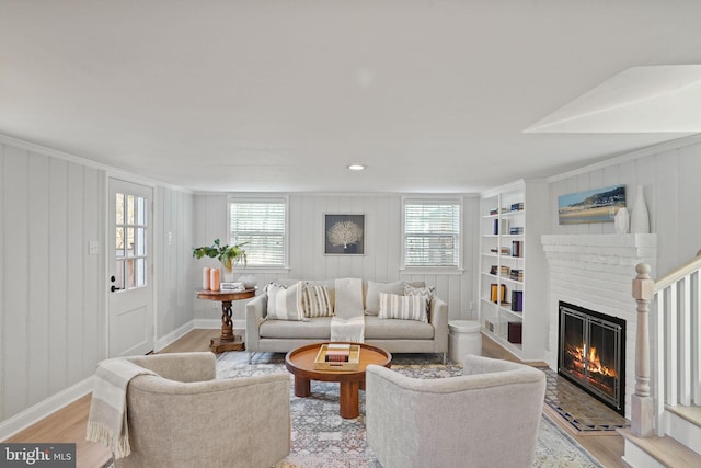 living area with a brick fireplace, built in features, baseboards, and light wood-type flooring