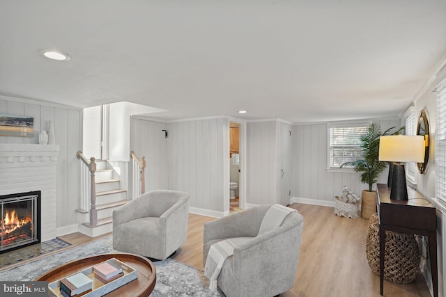 living area with stairway, a brick fireplace, wood finished floors, and baseboards