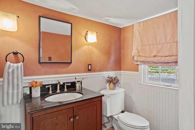 half bath featuring vanity, toilet, and wainscoting