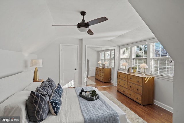 bedroom with a ceiling fan, vaulted ceiling, wood finished floors, and baseboards