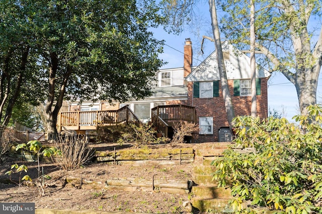 rear view of house with brick siding, a chimney, and a deck