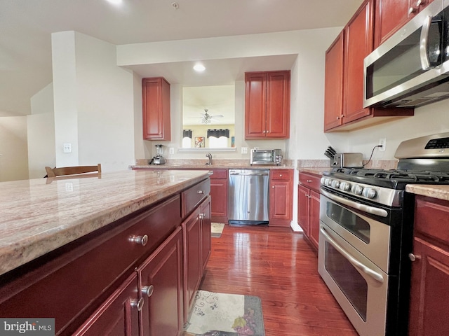 kitchen with dark brown cabinets, light stone countertops, appliances with stainless steel finishes, and dark wood-style floors