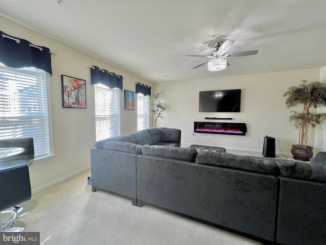 living room featuring a glass covered fireplace, baseboards, and a ceiling fan