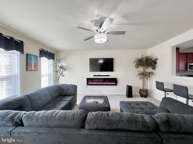 carpeted living room with a glass covered fireplace, baseboards, and ceiling fan