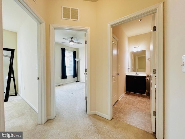 hallway featuring light tile patterned floors, visible vents, light carpet, and baseboards