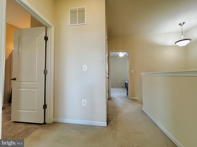 hall with visible vents, baseboards, and light colored carpet