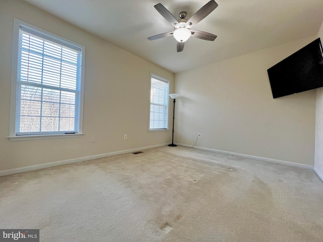 empty room with a ceiling fan, visible vents, light colored carpet, and baseboards