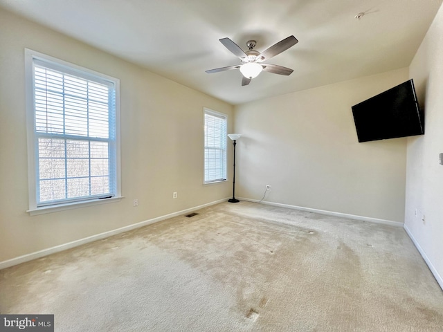 carpeted spare room featuring baseboards, visible vents, and ceiling fan