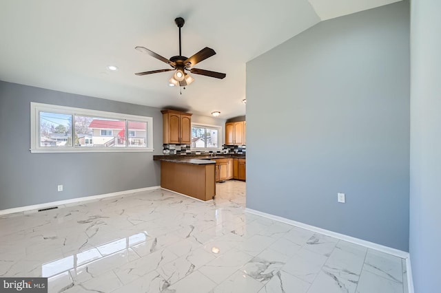 kitchen with marble finish floor, dark countertops, decorative backsplash, baseboards, and vaulted ceiling