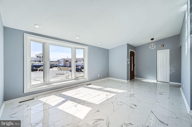 empty room with marble finish floor, a textured ceiling, baseboards, and lofted ceiling