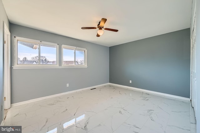 empty room with marble finish floor, a ceiling fan, and baseboards