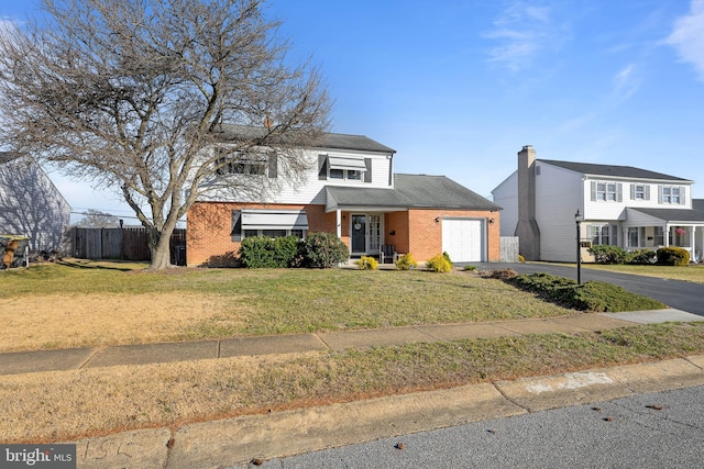 traditional-style home with a front yard, fence, driveway, a garage, and brick siding