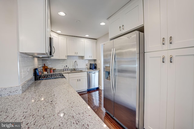 kitchen with a sink, dark wood finished floors, appliances with stainless steel finishes, white cabinets, and light stone countertops