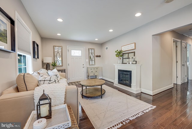 living area with a glass covered fireplace, recessed lighting, dark wood-style floors, and baseboards