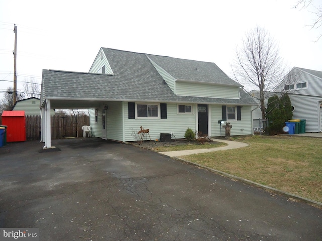 view of front of house with driveway, fence, roof with shingles, a front yard, and an attached carport