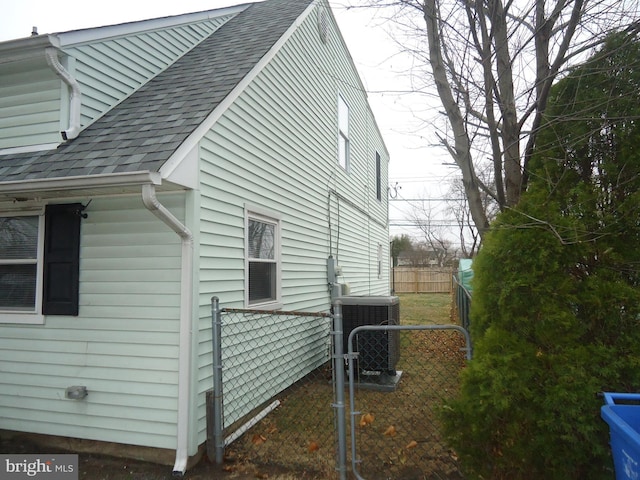 view of home's exterior with a gate, fence, central AC, and a shingled roof