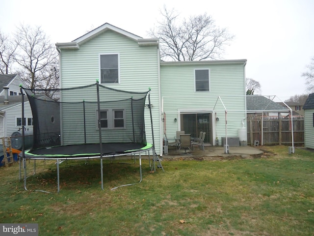 back of house featuring a patio area, a lawn, a trampoline, and fence