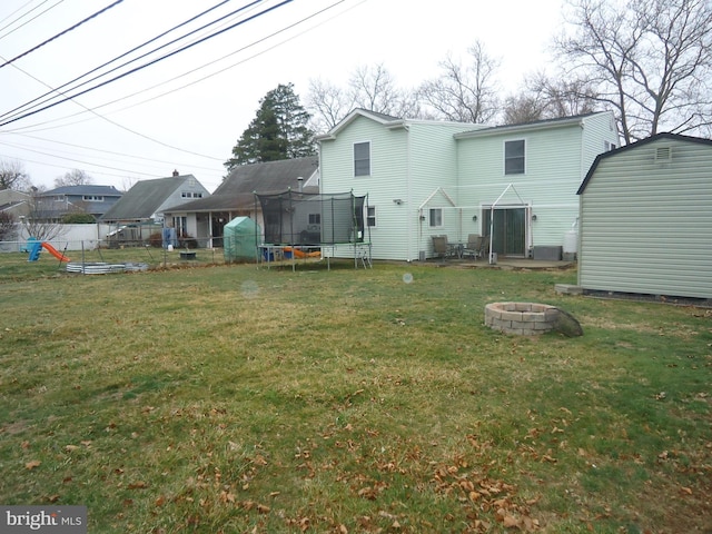 back of property featuring a yard, an outdoor fire pit, an outbuilding, and a trampoline