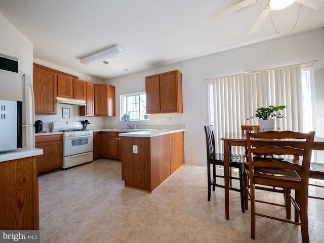 kitchen featuring white appliances, a peninsula, light countertops, under cabinet range hood, and brown cabinets