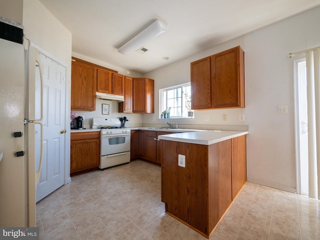 kitchen featuring white appliances, a peninsula, brown cabinets, and under cabinet range hood