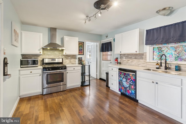 kitchen featuring a sink, stainless steel appliances, dark wood-type flooring, light countertops, and wall chimney range hood