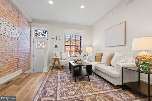 living area with visible vents, recessed lighting, brick wall, and wood finished floors