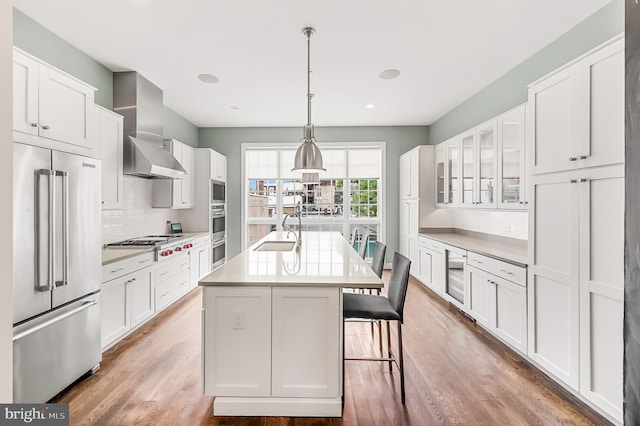 kitchen with wood finished floors, a sink, decorative backsplash, appliances with stainless steel finishes, and wall chimney range hood