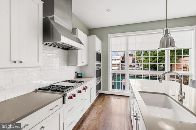 kitchen featuring tasteful backsplash, wall chimney range hood, appliances with stainless steel finishes, dark wood-style floors, and a sink