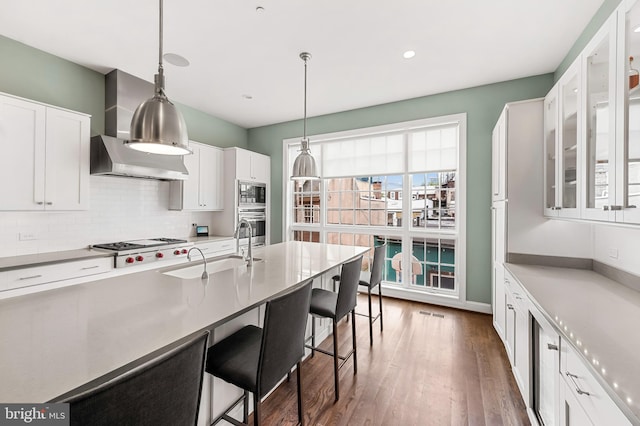 kitchen with backsplash, appliances with stainless steel finishes, white cabinetry, wall chimney exhaust hood, and a sink