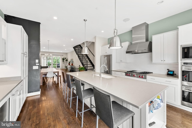 kitchen featuring backsplash, wall chimney range hood, dark wood finished floors, stainless steel appliances, and a sink